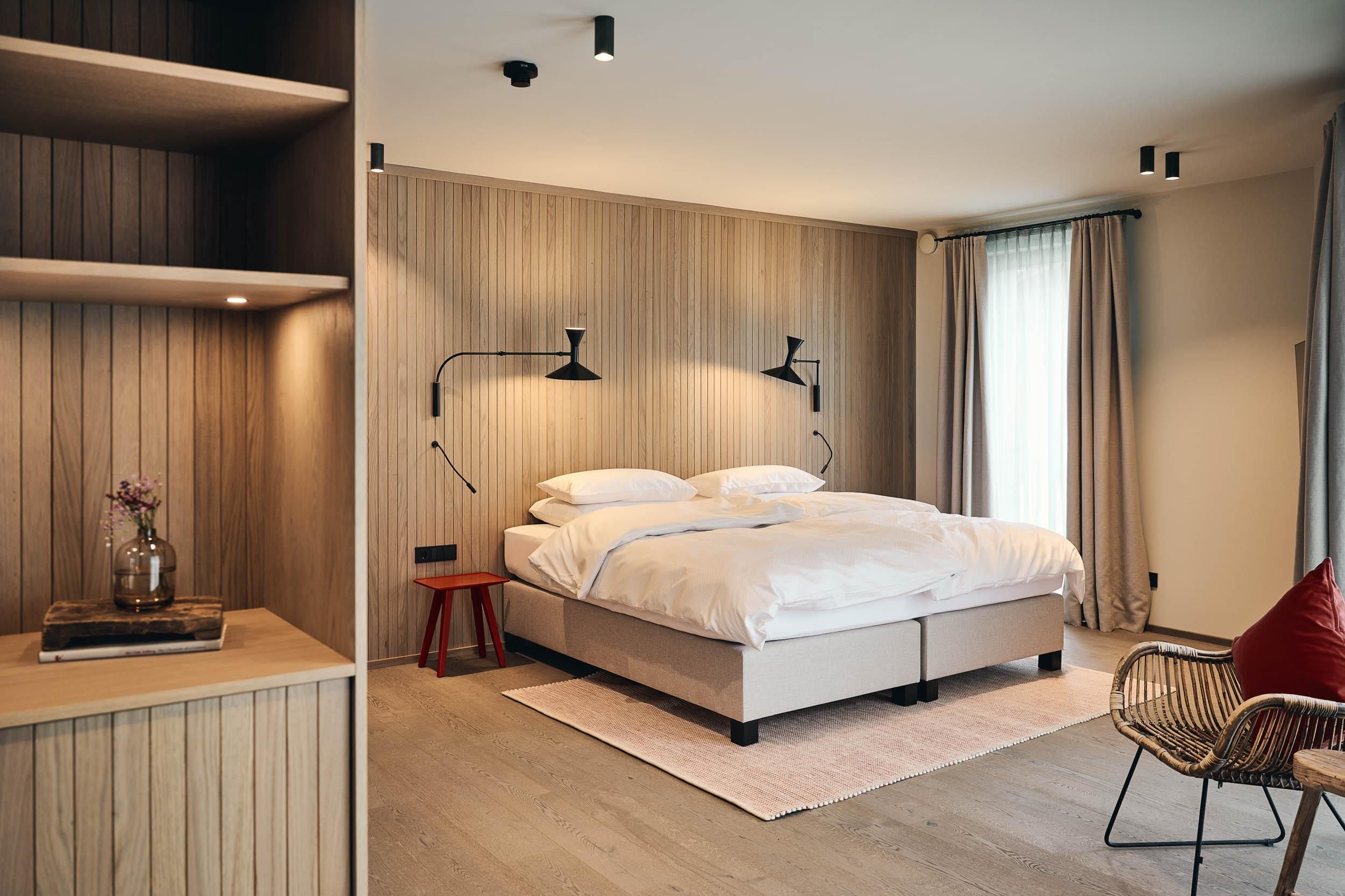 A modern bedroom with a large bed and warm wooden walls. The decor is stylish and comfortable, featuring a cozy seating area.